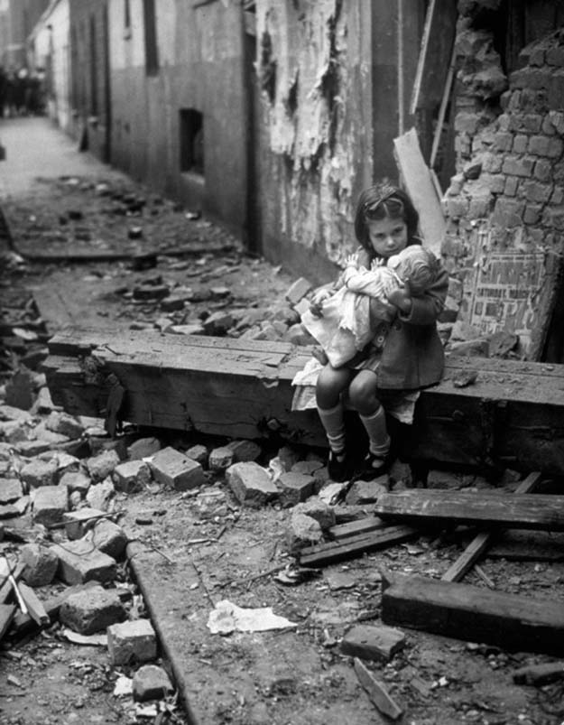 Little girl comforting her doll in the ruins of her bomb damaged home, London, 1940