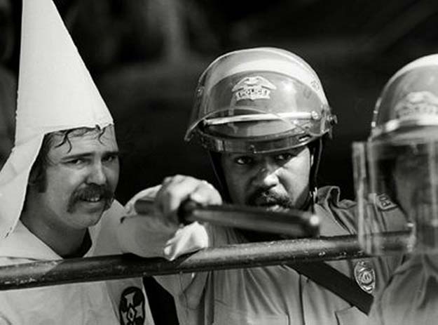 Police officer protects a KKK member from protestors