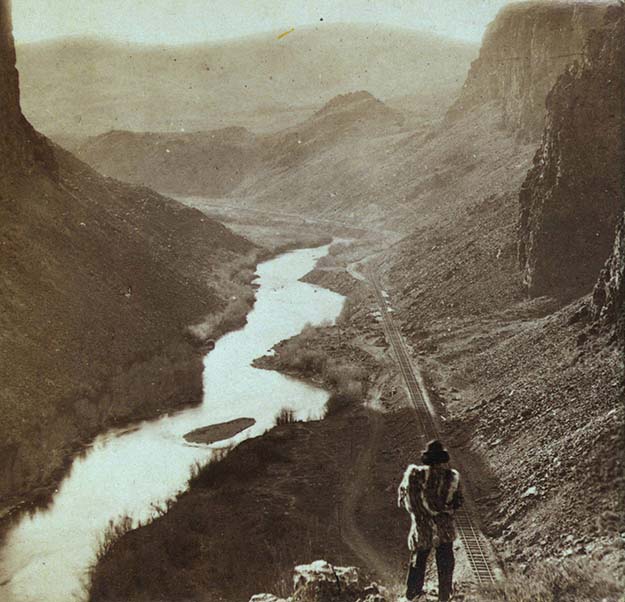 A Native American looks down at a newly-completed section of the transcontinental railroad. Nevada, about 1868