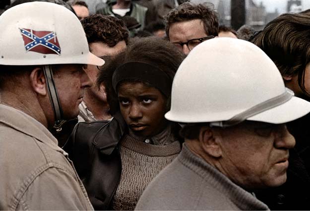 A Civil Rights demonstration in the 60s, an african-american woman stares down a man donning the Confederate flag on his hard-hat, Bob Adelman photograph